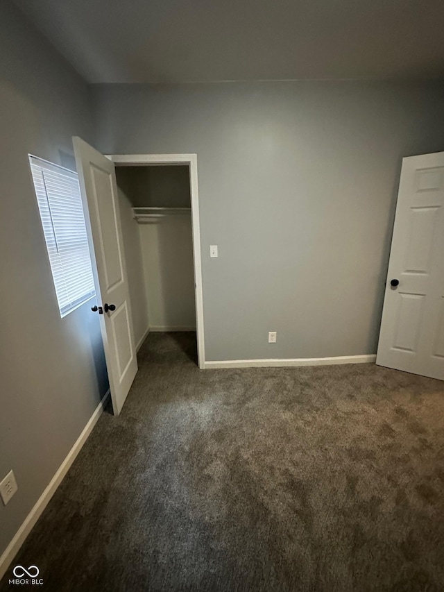 unfurnished bedroom featuring dark carpet, baseboards, and a closet