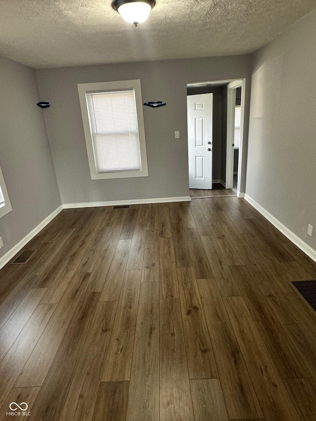 spare room featuring dark wood finished floors, a textured ceiling, and baseboards