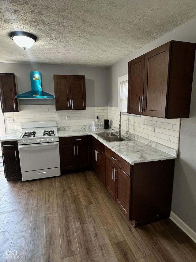 kitchen with wall chimney range hood, white range with gas cooktop, a sink, dark wood-style floors, and light countertops