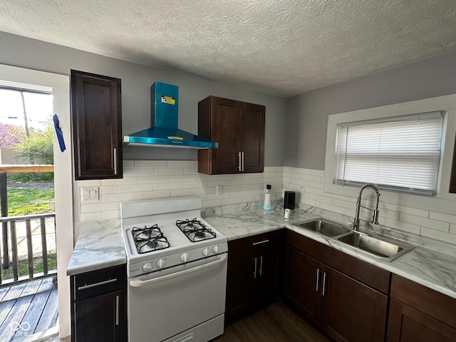 kitchen with wall chimney exhaust hood, white range with gas cooktop, a sink, decorative backsplash, and plenty of natural light