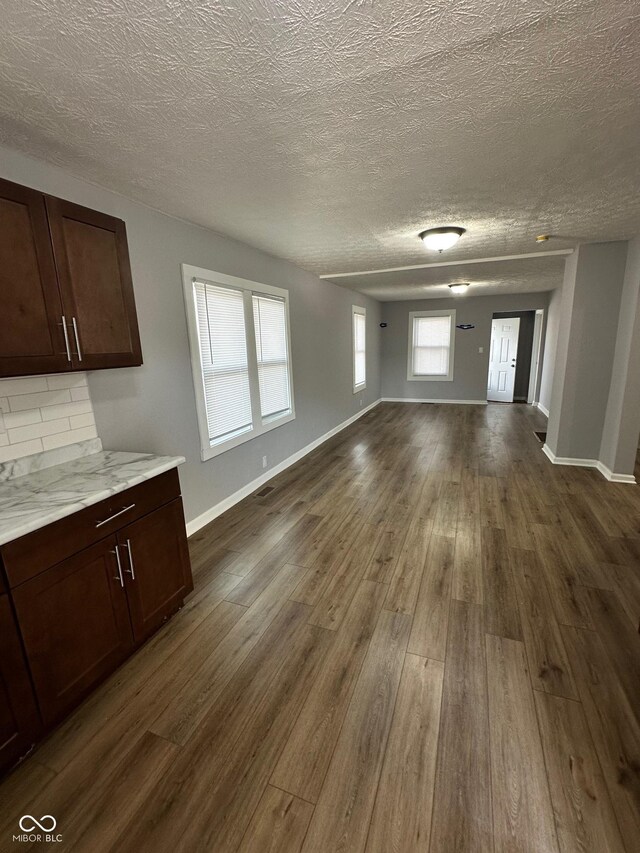 unfurnished dining area featuring dark wood finished floors, baseboards, and a textured ceiling