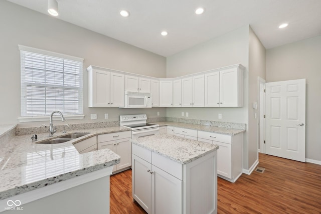 kitchen with white appliances, a sink, wood finished floors, white cabinetry, and recessed lighting