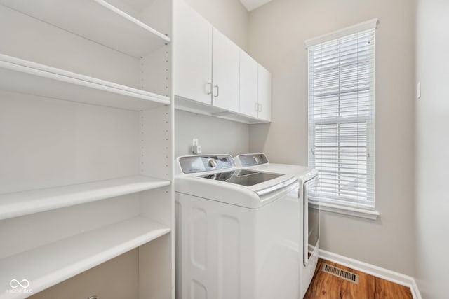 washroom featuring washing machine and clothes dryer, cabinet space, baseboards, wood finished floors, and healthy amount of natural light