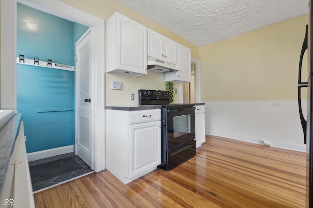 kitchen with black appliances, under cabinet range hood, light wood finished floors, white cabinetry, and dark countertops