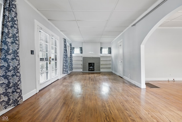 unfurnished living room with arched walkways, wood finished floors, a fireplace with raised hearth, and baseboards