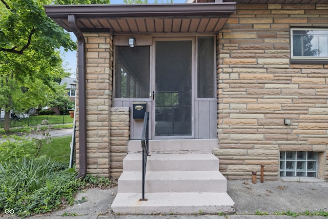 doorway to property with stone siding and fence