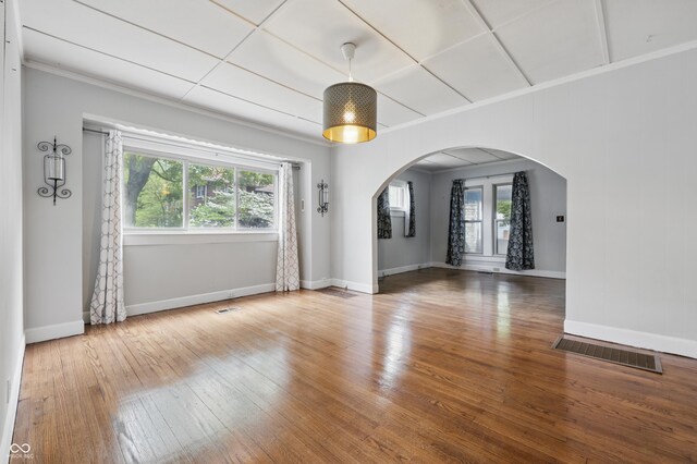 spare room featuring arched walkways, healthy amount of natural light, hardwood / wood-style floors, baseboards, and crown molding