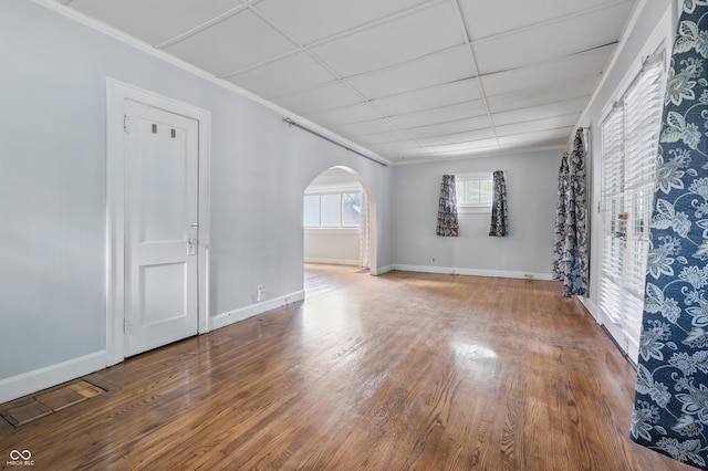 empty room featuring arched walkways, wood finished floors, baseboards, and crown molding