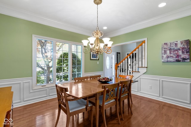 dining area featuring a wainscoted wall, a decorative wall, ornamental molding, a chandelier, and wood finished floors
