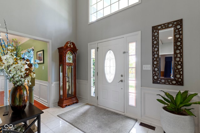 entryway featuring light tile patterned floors, wainscoting, a decorative wall, and a high ceiling