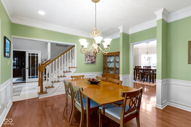 dining area with a chandelier, crown molding, wood finished floors, wainscoting, and stairway