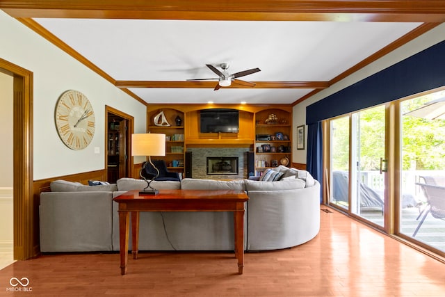 living room featuring ornamental molding, a glass covered fireplace, ceiling fan, wood finished floors, and built in features
