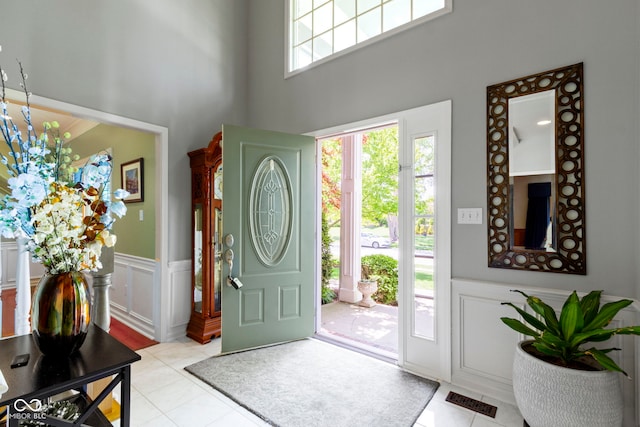 entryway featuring light tile patterned floors, a towering ceiling, a wainscoted wall, and a decorative wall