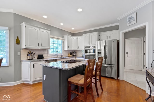 kitchen featuring stainless steel appliances, a sink, white cabinetry, light wood-style floors, and ornamental molding