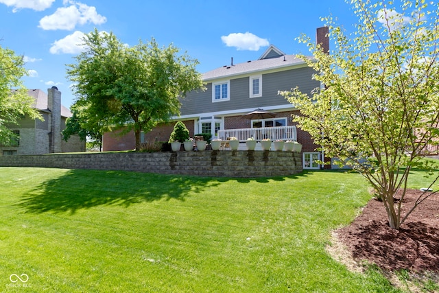 back of property featuring a lawn, a chimney, and brick siding