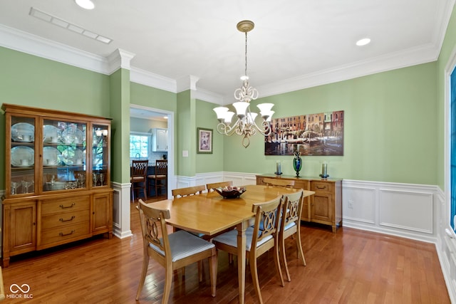dining space with wood finished floors, ornamental molding, wainscoting, a chandelier, and a decorative wall