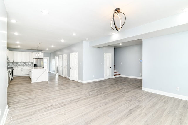 unfurnished living room featuring light wood-type flooring, recessed lighting, baseboards, and stairs