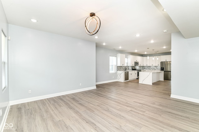 unfurnished living room with a sink, light wood-style floors, baseboards, and recessed lighting