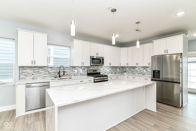 kitchen featuring appliances with stainless steel finishes, a sink, light wood-style floors, white cabinets, and decorative backsplash