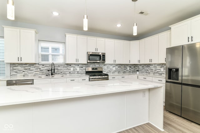 kitchen with appliances with stainless steel finishes, a sink, light wood finished floors, white cabinetry, and backsplash