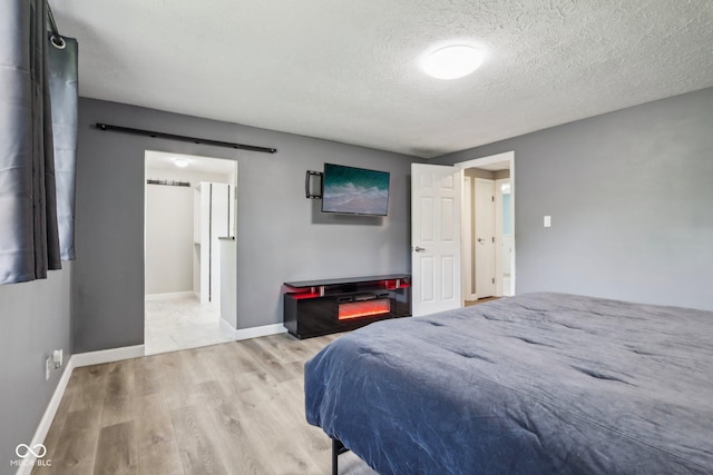 bedroom with wood finished floors, a textured ceiling, a barn door, and baseboards