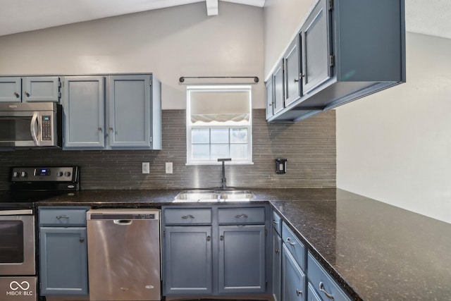 kitchen with stainless steel appliances, a sink, tasteful backsplash, gray cabinetry, and lofted ceiling