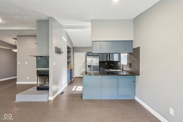 kitchen featuring stainless steel fridge, a sink, a peninsula, a multi sided fireplace, and baseboards