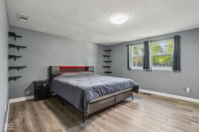 bedroom with a textured ceiling, wood finished floors, and baseboards