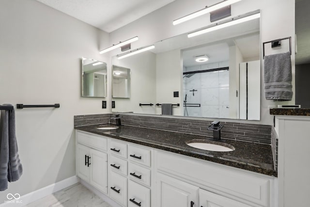 full bath with marble look tiles, baseboards, a marble finish shower, and double vanity