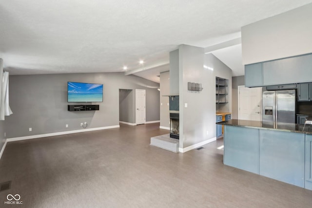 kitchen featuring stainless steel fridge, open floor plan, vaulted ceiling, baseboards, and a multi sided fireplace