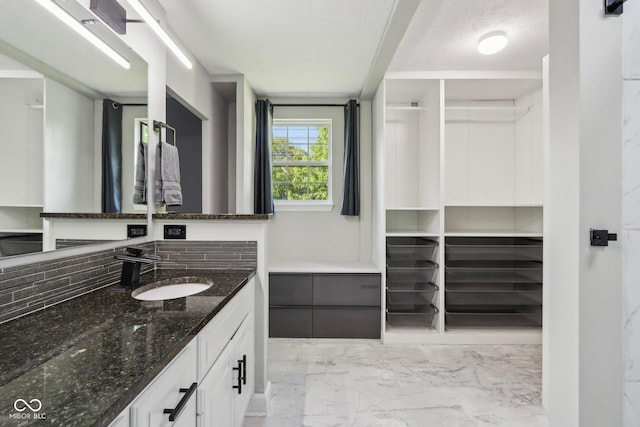 bathroom with marble finish floors, vanity, tasteful backsplash, and a walk in closet
