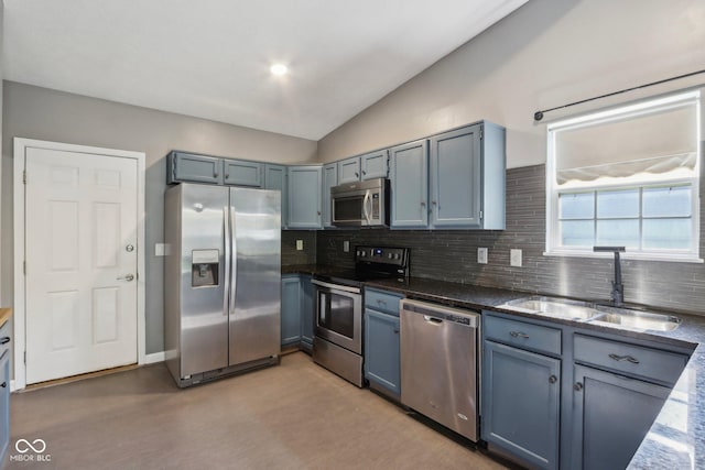 kitchen featuring appliances with stainless steel finishes, a sink, tasteful backsplash, lofted ceiling, and dark stone countertops