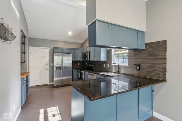 kitchen with appliances with stainless steel finishes, a sink, a peninsula, dark stone countertops, and decorative backsplash