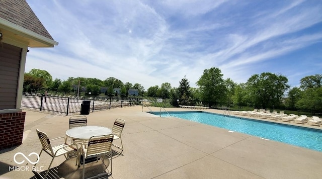 community pool with a patio area, fence, and view of scattered trees