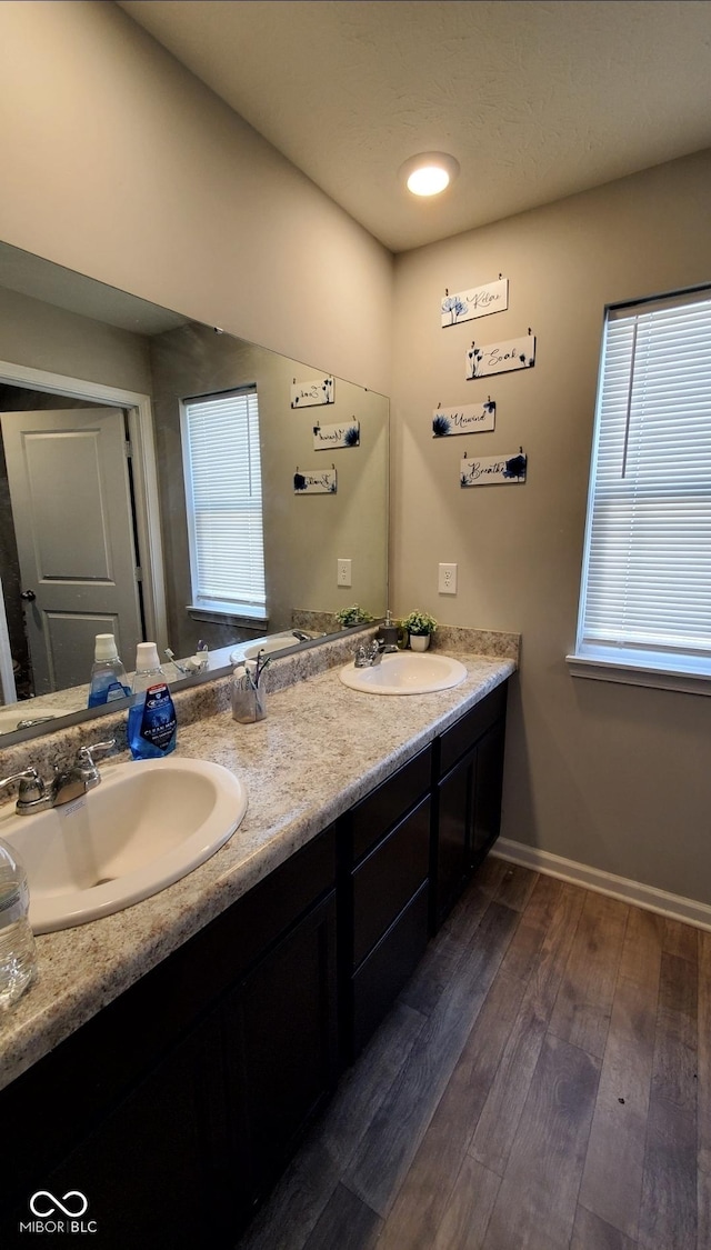 full bath with wood finished floors, double vanity, and baseboards