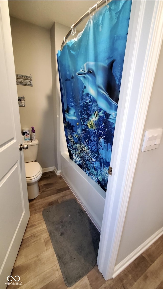 full bath with wood finished floors, toilet, baseboards, and shower / bath combination with curtain