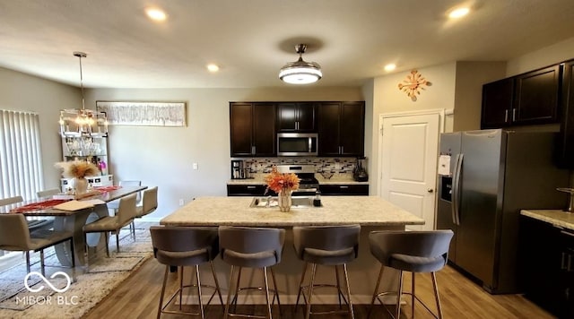 kitchen featuring appliances with stainless steel finishes, light wood-style floors, a kitchen breakfast bar, tasteful backsplash, and recessed lighting