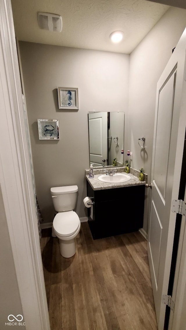 half bath with wood finished floors, toilet, vanity, and baseboards