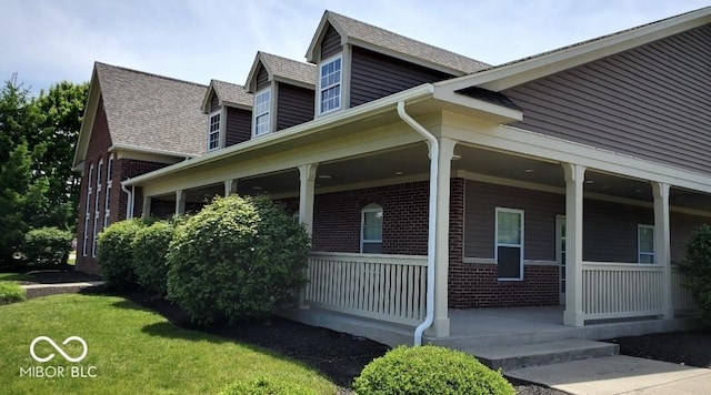 view of side of property with covered porch, brick siding, and a shingled roof
