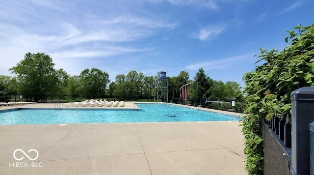 community pool with a patio, view of scattered trees, and fence