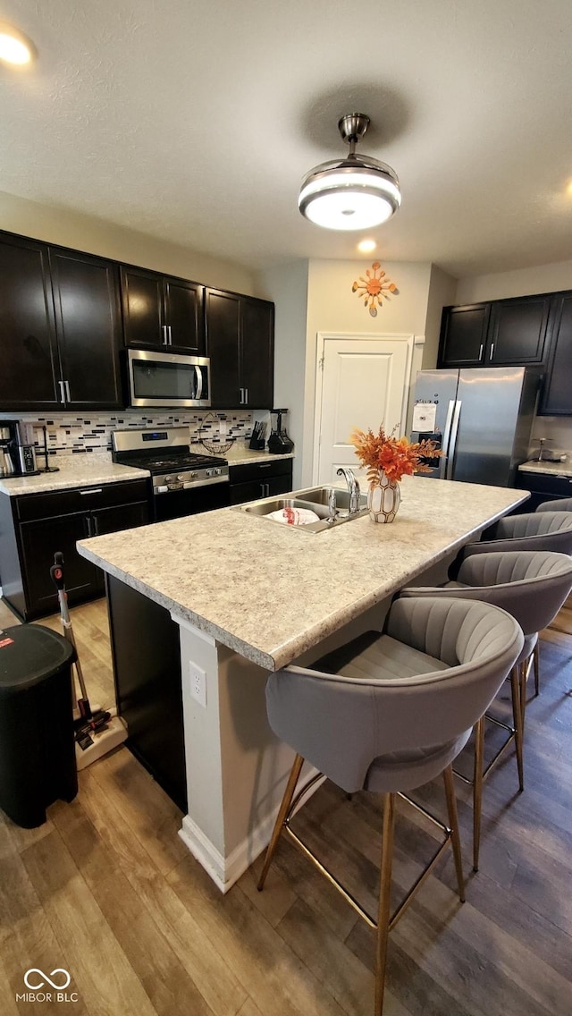 kitchen with appliances with stainless steel finishes, dark cabinetry, a sink, a kitchen breakfast bar, and decorative backsplash