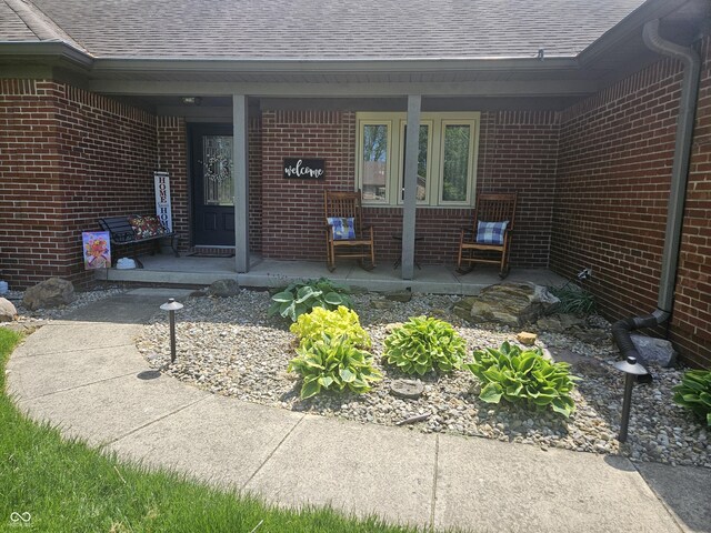 doorway to property with roof with shingles, covered porch, and brick siding