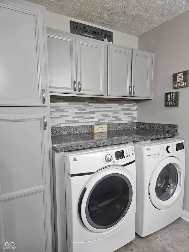 laundry area with washing machine and clothes dryer, cabinet space, light tile patterned floors, and a textured ceiling