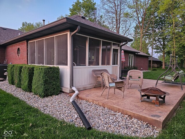 view of side of property featuring a fire pit, a patio area, a sunroom, roof with shingles, and brick siding