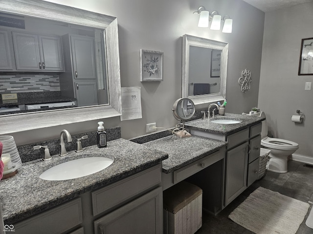 bathroom with toilet, tasteful backsplash, two vanities, and baseboards