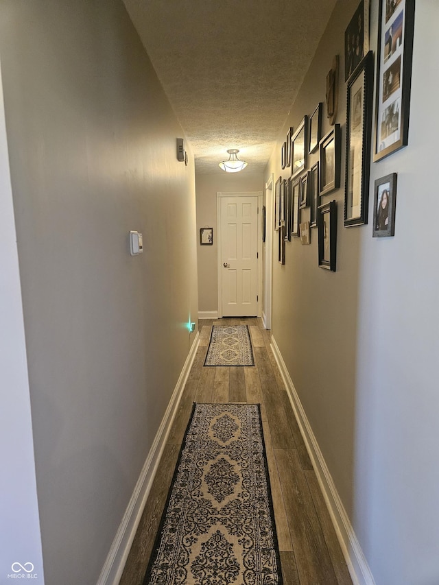 hallway featuring dark wood-style floors, a textured ceiling, and baseboards