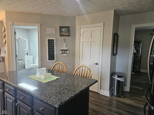 kitchen featuring dark wood-style floors, freestanding refrigerator, blue cabinetry, a center island, and a textured ceiling