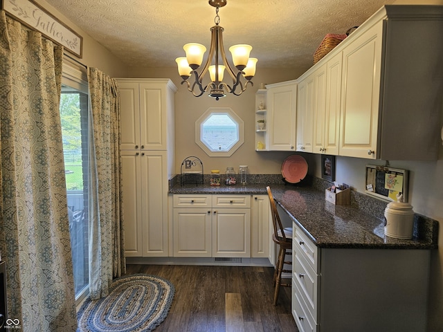 kitchen with dark wood finished floors, a chandelier, a textured ceiling, decorative light fixtures, and white cabinets