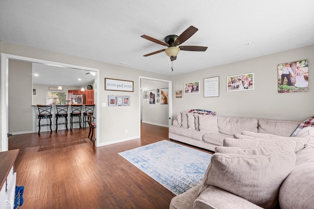 living room with a ceiling fan, wood finished floors, baseboards, and bar