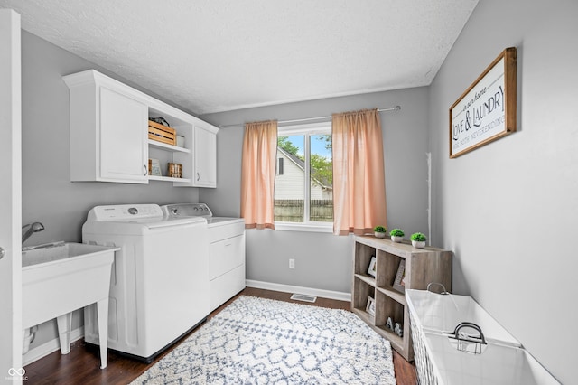 clothes washing area featuring washing machine and dryer, cabinet space, a textured ceiling, dark wood-style flooring, and baseboards
